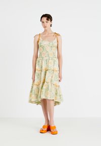 Bloemenprint jurk in pastelgroen en geel, met een gelaagde rimpelrok en verstelbare schouderbanden. Gecombineerd met feloranje platform sandalen.