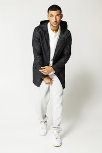 Black waterproof jacket with a hood, layered over a white polo shirt, paired with light grey sweatpants and white sneakers.