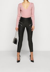 Rosa ribbad långärmad topp med djup V-ringning, kombinerad med svart, högmidjad byxa i fejkskinn med blixtlåsfickor och smal passform.