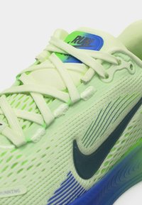 Ανοιχτό πράσινο παπούτσι τρεξίματος Nike με άσπρα κορδόνια, μαύρο λογότυπο swoosh, μπλε λεπτομέρειες και ετικέτα «RUN» στη γλώσσα.