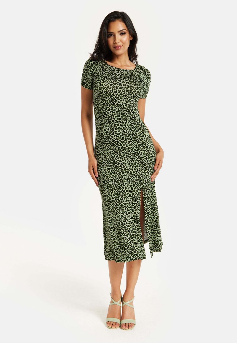 Green leopard print dress with short sleeves and a side slit. Soft fabric, fitted design, and knee-length hem. Paired with green strappy sandals.