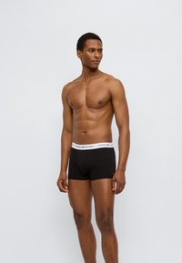 Μαύρα boxer briefs με λευκή ελαστική μέση που φέρει το λογότυπο "Tommy Hilfiger". Το ύφασμα φαίνεται λείο και εφαρμοστό, τονίζοντας το σχήμα.