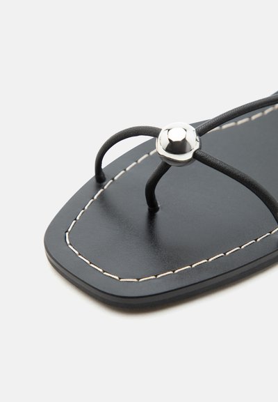 Μαύρο σανδάλι με τετράγωνη μύτη και λεπτά λουράκια που συνδέονται με ασημί μεταλλικό κουμπί και λευκή ραφή κατά μήκος της άκρης της σόλας.