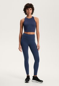 Sötétkék sport crop top és magas derekú leggings rugalmas anyagból, fekete sportcipővel párosítva. Simább, testhezálló kialakítás.