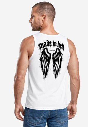 Mann mit kurzen Haaren, der ein weißes ärmelloses Shirt mit schwarzem Flügeldesign und dem Text "made in hell" auf dem Rücken trägt, kombiniert mit blauen Jeans.