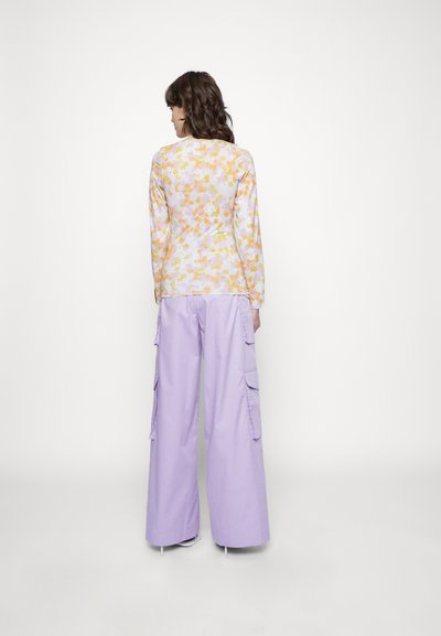 Camisola de mangas longas com um padrão floral em amarelo e laranja sobre um fundo rosa claro, combinada com calças cargo largas em lavanda.