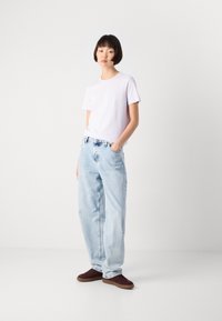 Lys lilla bomulls T-skjorte kombinert med løse lyseblå denim jeans. Modellen har på seg mørkebrune joggesko. Minimalistisk design med sidelommer.