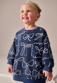 Sweatshirt bleu marine avec motifs de nœuds blancs, col rond, et poignets côtelés. Ourlet arrondi et coupe décontractée adaptée aux enfants.