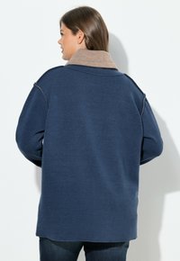 Granatowy, oversize'owy sweter z kontrastującym beżowym kołnierzem, wykonany z miękkiego, teksturowanego materiału; posiada widoczne przeszycia wzdłuż szwów.