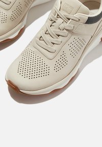 Lichtbeige sportschoenen met een geperforeerd ontwerp, textuur van synthetisch materiaal, platte veters en een contrasterende bruine rubberen zool.