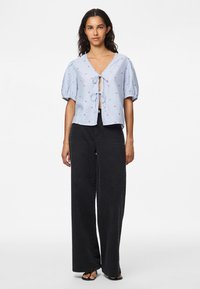 Blue striped blouse with puff sleeves and a tie closure, featuring small red floral patterns. Paired with wide black pants.