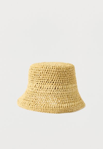 Chapeau seau tissé en paille jaune avec un motif à tissage ouvert et un bord légèrement évasé sur un fond neutre.