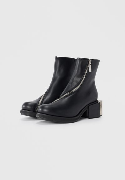 Black leather ankle boots with a zipper closure, square block heel, and a metallic accent on the heel. Smooth texture and sleek design.