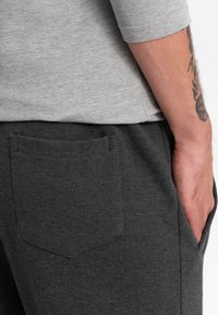 Camisa de manga larga gris sobre pantalones jogger gris oscuro con un bolsillo trasero visible, que presentan una textura suave y un diseño limpio y sencillo.