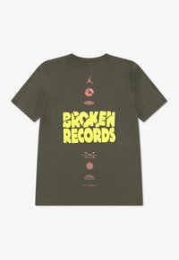 Λαδί πράσινο μπλουζάκι με στρογγυλή λαιμόκοψη. Διαθέτει έντονο κίτρινο κείμενο "BROKEN RECORDS" και διάφορα γραφικά εικονίδια σε ροζ, όπως ένα μπάσκετ και μια υδρόγειο σφαίρα.