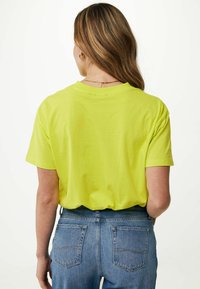 Krátký rukáv, jasně žluté tričko vyrobené z měkké látky, uvolněný střih, s kulatým výstřihem. Stylizované s džínami s vysokým pasem v modré barvě.