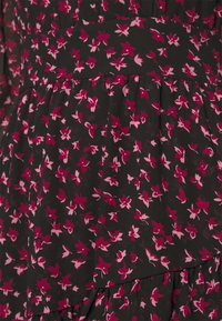 Zwarte stof met een bloemenpatroon met kleine roze en rode bloemen, gelaagd ontwerp, gladde textuur en taillebanddetail.