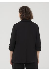 Giacca nera con maniche a tre quarti, cuciture frontali e polsini arrotolati. Tessuto liscio con un colletto strutturato e dettaglio di spacco posteriore.