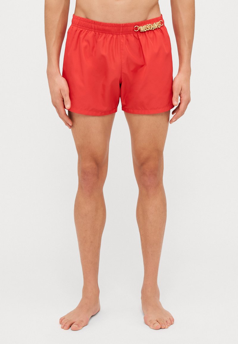 Shorts de bain rouges en matériau léger, dotés d'une taille élastique avec un accent de logo doré. Forme classique, ajustée, au-dessus du genou.