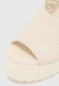 Sandale ouverte beige avec une tige en daim doux, une épaisse semelle blanche et des détails de couture minimaux. Le design est élégant et moderne.