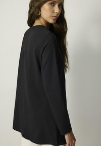 Maglietta nera a maniche lunghe con una vestibilità rilassata, caratterizzata da un colletto rotondo e fessure laterali. Tessuto morbido e design minimalista.