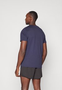 Chemise à manches courtes bleu marine en coton. Design simple avec un col rond et un ourlet droit. Portée avec un short de sport noir.