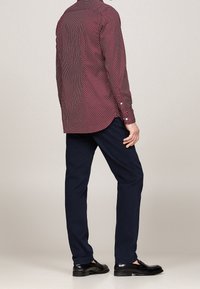 Rood-wit gestreept overhemd met een button-down kraag, gecombineerd met donkerblauwe broeken en zwarte schoenen, gezien vanuit de achterkant.