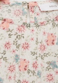 Tessuto floreale color crema con fiori rosa, blu e verdi. Presenta una chiusura a occhiello sul retro e una consistenza morbida e leggera.