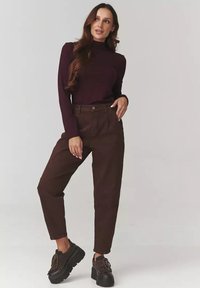 Brązowe spodnie o wysokim stanie w luźnym kroju, połączone z dopasowanym bordowym golfem. Obuwie charakteryzuje się grubą podeszwą i ciemnymi sznurowadłami.