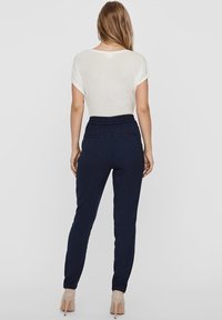 Granatowe spodnie dresowe z elastycznym paskiem i dwiema tylnymi kieszeniami, zestawione z lekką białą bluzką z krótkim rękawem.