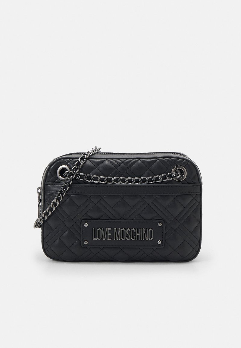 Melnā pītā crossbody soma ar sudraba ķēdes siksnu, priekšpusē ar taisnstūra logotipa plāksni un ar rāvējslēdzēju.