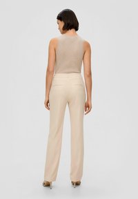 Beige mouwloze top gecombineerd met lichtbeige op maat gemaakte broek. De broek heeft zakken en een recht model. Over het geheel een gladde structuur.