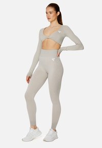 Hellgraues Sportbekleidungsset bestehend aus einem langärmligen, cropped Oberteil mit tiefem V-Ausschnitt und hochtaillierten Leggings mit strukturierter Musterung.