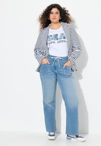 Randig blazer i svart och vitt över en vit grafisk t-shirt. Ljusblå vida jeans med elastiskt midjeband och fickor. Blå sneakers.