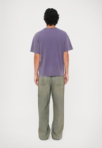 Tricou cu mânecă scurtă, guler tip crew, într-o nuanță de violet estompat, asortat cu blugi largi, de culoare verde deschis, care au cusături vizibile și buzunare.