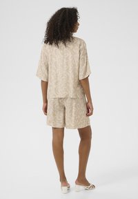 Haut à manches courtes beige et shorts assortis avec un motif tourbillonnant blanc, fabriqués en tissu léger, avec une coupe décontractée et des fentes sur les côtés.