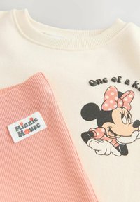 Krämfärgad sweatshirt med en Minnie Mouse-grafik och text. Inkluderar en rosa ribbad manschett med en "Minnie Mouse"-etikett. Mjuk bomullsmaterialblandning.