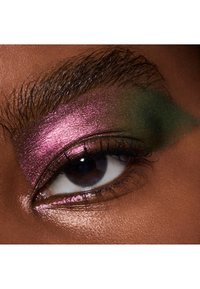 Nærbillede af et øje med markant, glitrende pink og grøn øjenskygge, mørke øjenvipper og en glat hudstruktur.