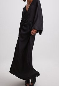 Černé dlouhé šaty s hlubokým výstřihem do V, nařasením a kapsami. Vyrobeno z hladkého, splývavého materiálu. Elegantní a minimalistický design.