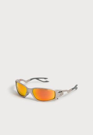 Lunettes de sport à monture argentée avec verres orange miroir enveloppants et embouts de branches noirs en caoutchouc sur fond blanc.