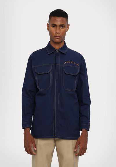 Giacca camicia blu navy in cotone, con due tasche sul petto, cuciture arancioni a contrasto e "JAFFA" ricamato sul lato sinistro.