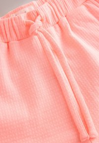 Shorts rose clair avec une taille élastique et un cordon de serrage noué. Tissu texturé avec de petits points en relief pour un détail supplémentaire.