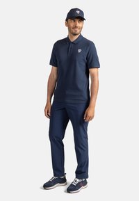 Námořnické polo tričko s límečkem a logem, spárované s odpovídajícími kalhotami a námořnickými teniskami s bílými akcenty. Ukázka casual outfitu.