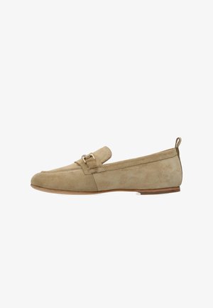 Mocasines de ante beige con suela plana, punta redondeada y una correa decorativa con una pequeña hebilla metálica. Superficie texturizada y diseño minimalista.