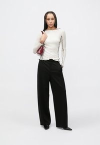 Top alb cu mâneci lungi și margini negre ondulate, asortat cu pantaloni evazați negri și o geantă mică burgundă. Textură netedă a țesăturii.