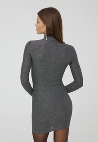 Mini abito grigio aderente in un tessuto a maglia luccicante, con maniche lunghe e scollatura alta, dalla texture liscia e silhouette elegante.