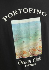 Juodas marškinėliai su spalvingu paplūdimio vaizdu, atspausdintu priekyje, su užrašu "Portofino Ocean Club Premium" viršuje ir apačioje.