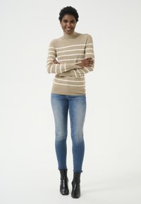 Vaalea raidallinen pooloneule, jossa on vaalean kreemiväriset raitoja, istuva malli. Yhdistetty sinisiin kapeisiin farkkuihin ja mustiin nilkkabootseihin. Silkkinen tekstuuri.