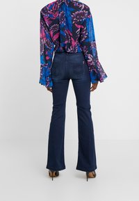 Blusa de estampado floral con mangas acampanadas en azul marino, combinada con jeans acampanados de mezclilla oscura que cuentan con bolsillos traseros y un ajuste entallado.