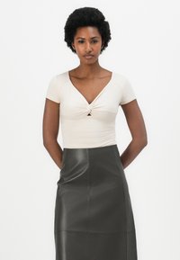 Lys beige tettsittende topp med korte ermer og knyttet frontdetalj, kombinert med et høyt livsort skinnskjørt med glatt finish.